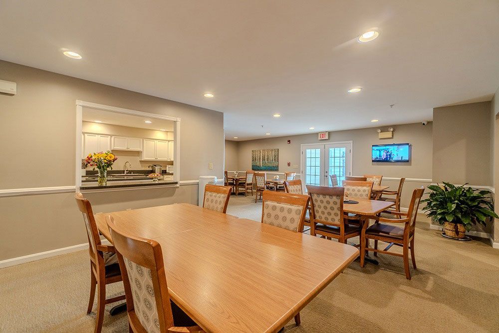 Spacious dining room with wooden tables, chairs, recessed lighting, and a wall-mounted TV.