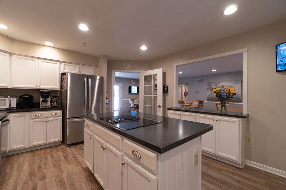 Modern kitchen with white cabinets, stainless steel fridge, black island countertop, and open pass-through window