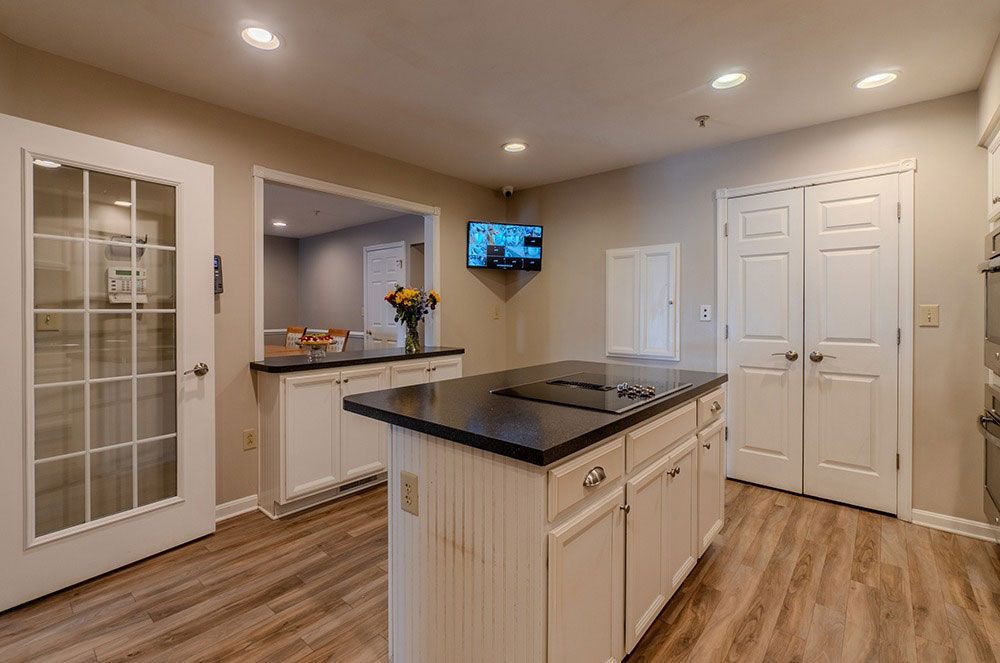 Modern kitchen with island, white cabinets, dark countertops, wood floors, and wall-mounted TV
