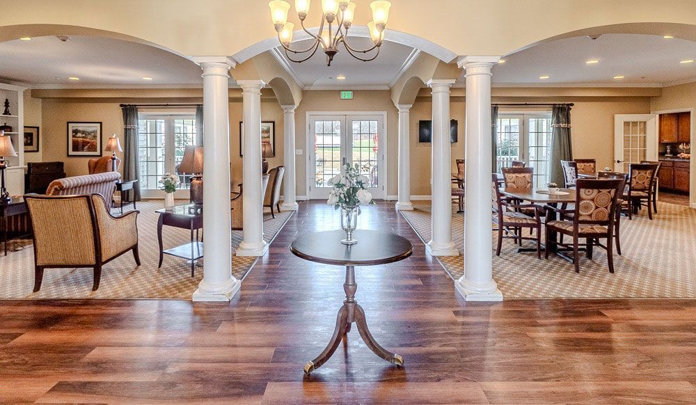 Elegant open living room with white columns, hardwood floors, chandelier, and dining area in the background