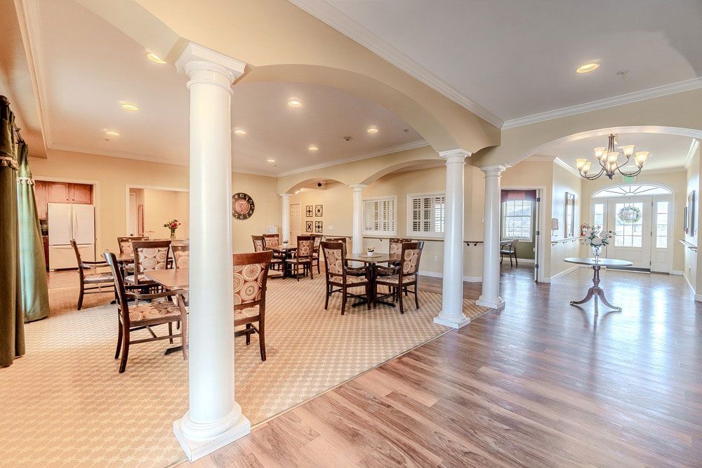 Bright open dining room with white columns, wooden tables, tile floor, and hardwood foyer area