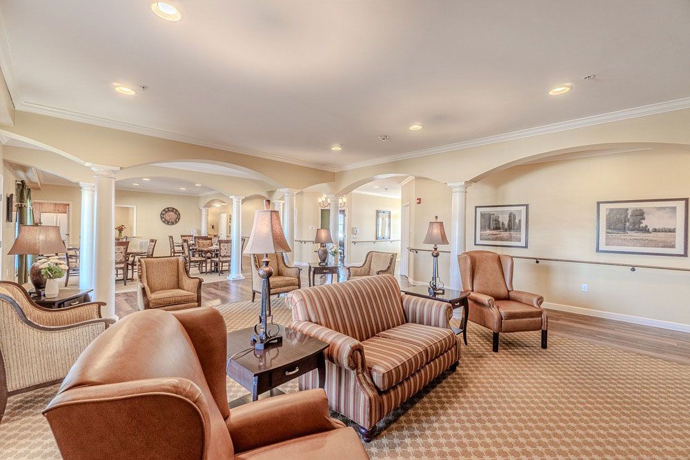 Spacious beige living room with upholstered armchairs, sofas, framed art, and recessed ceiling lights.