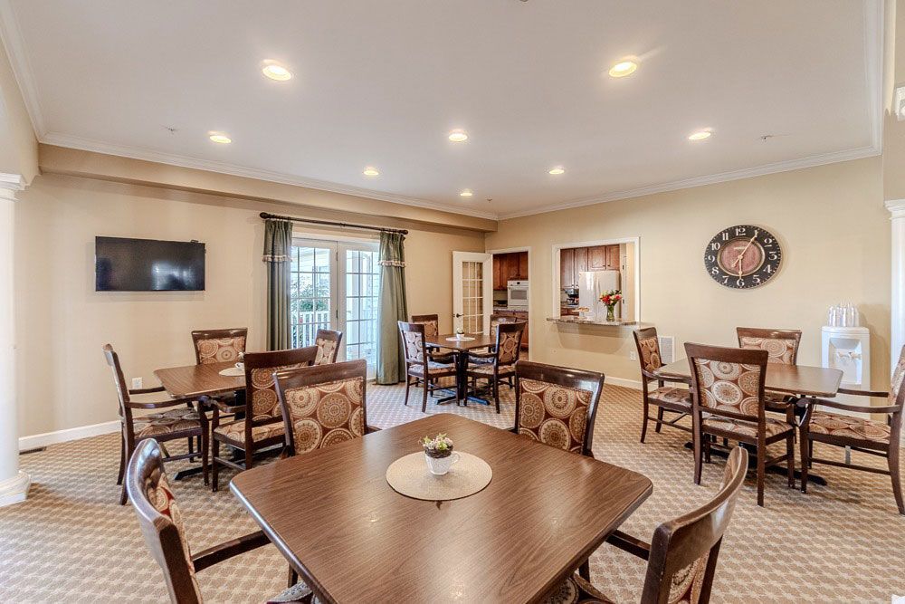 Spacious dining room with multiple wooden tables, chairs, and a wall-mounted TV under recessed lighting.