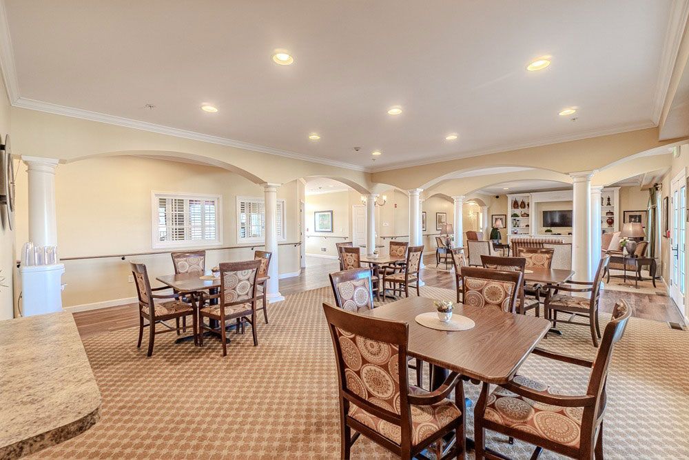Bright dining hall with tables, chairs, and recessed ceiling lights in a beige carpeted room