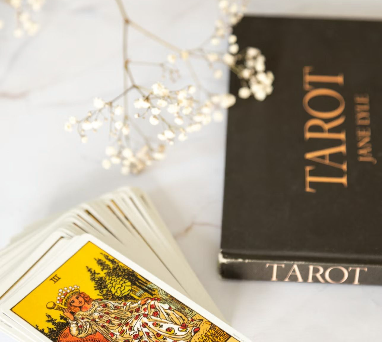 Tarot cards beside a black tarot box with gold lettering on a light marble surface