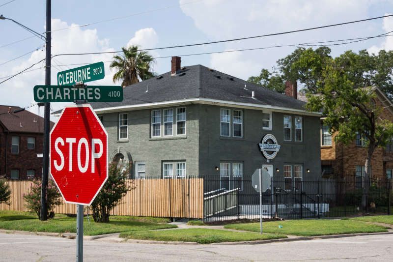Stop sign at a street corner with a two-story green building and street signs for Cleburne and Chartres.