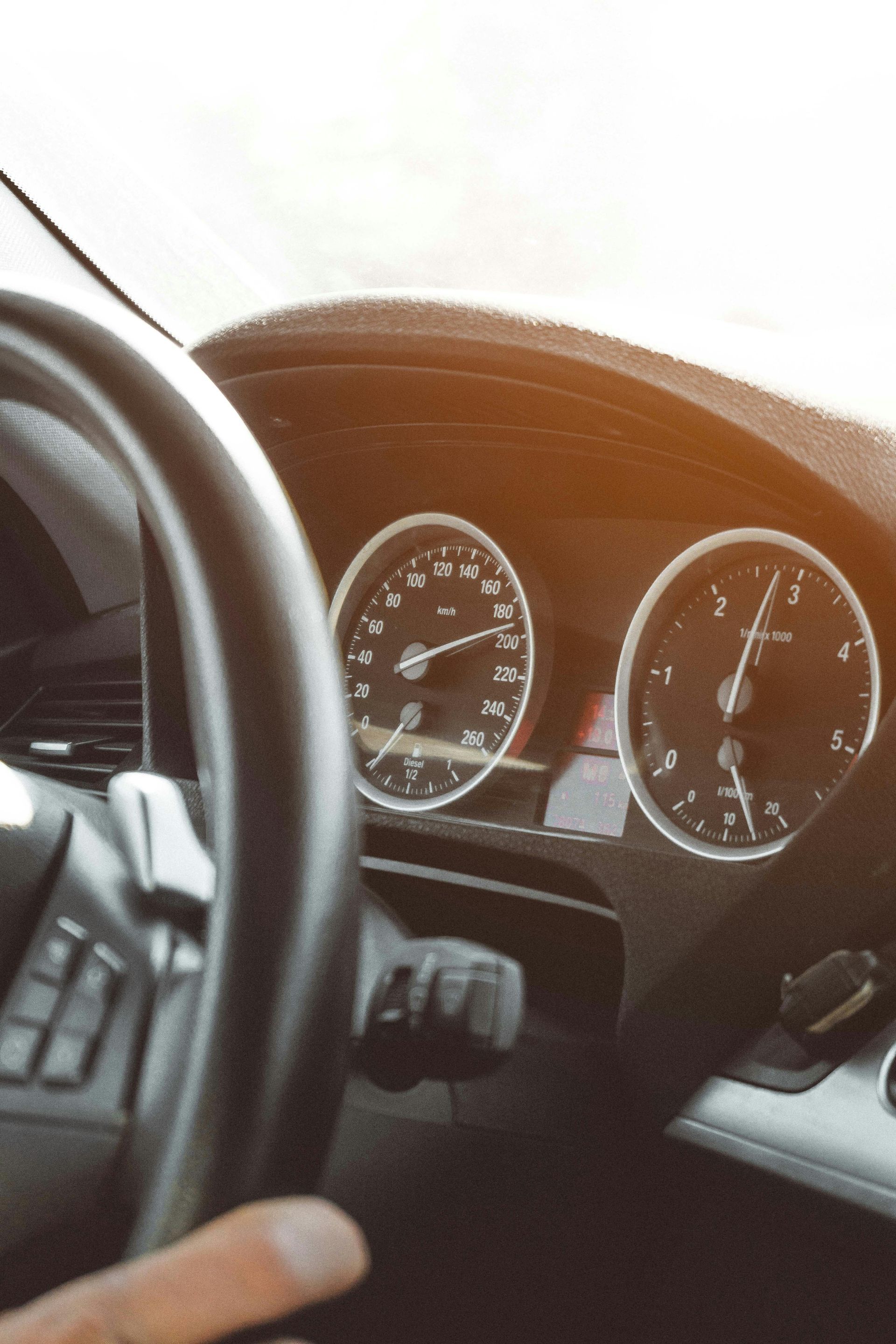 Car dashboard with gauges and steering wheel, sun shining.