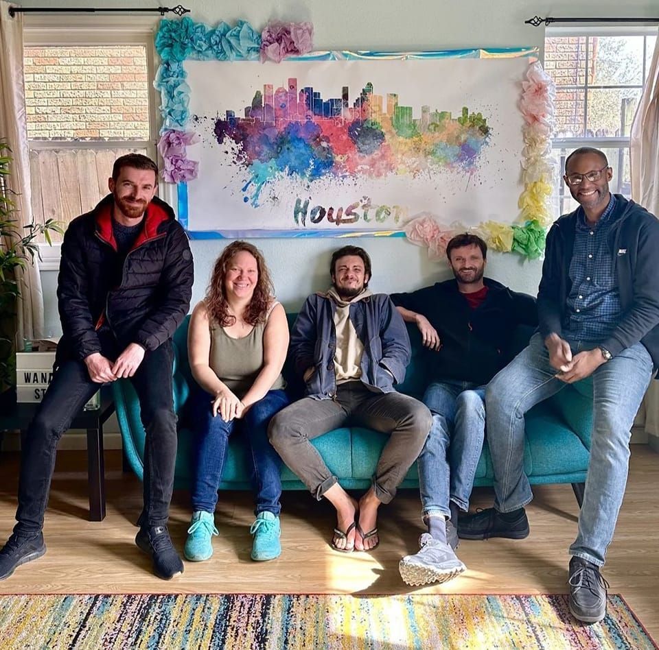 Five people seated on a teal couch in front of a Houston skyline painting, smiling.