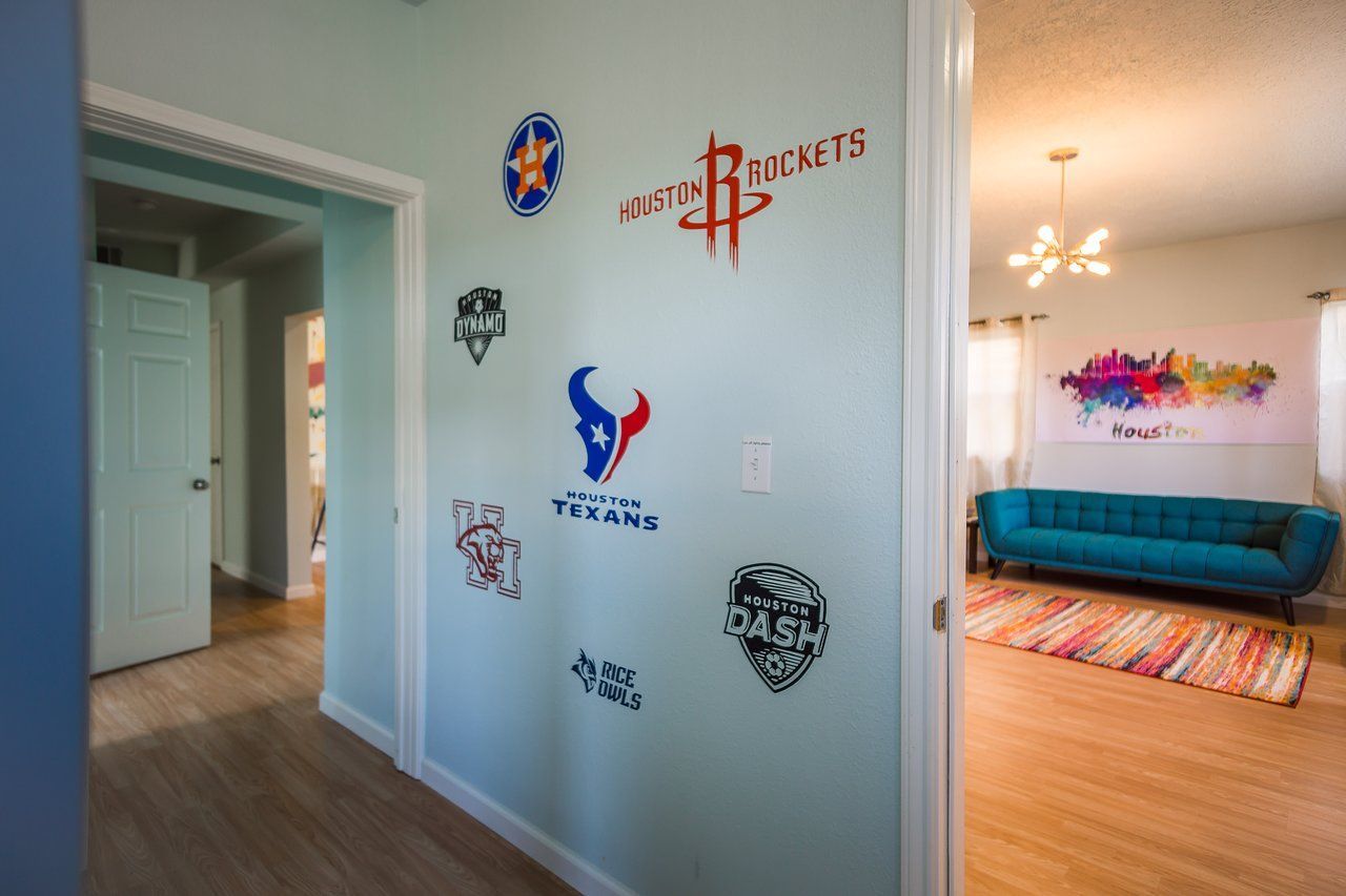 Hallway with sports team logos on a light blue wall, leading to a living room with a turquoise sofa and artwork.