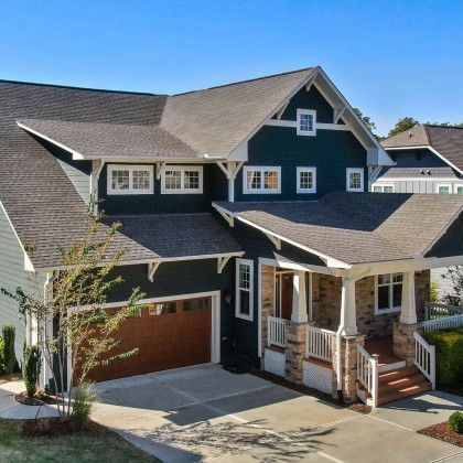 Two-story Craftsman-style house with dark blue siding, brown garage door, and a covered porch.
