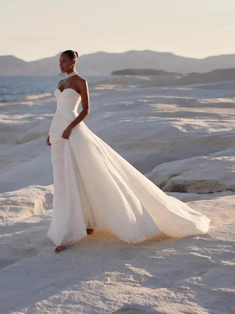 A woman in a white wedding dress is standing on a beach.
