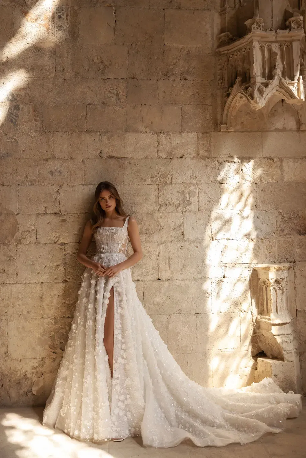A woman in a wedding dress is leaning against a brick wall.