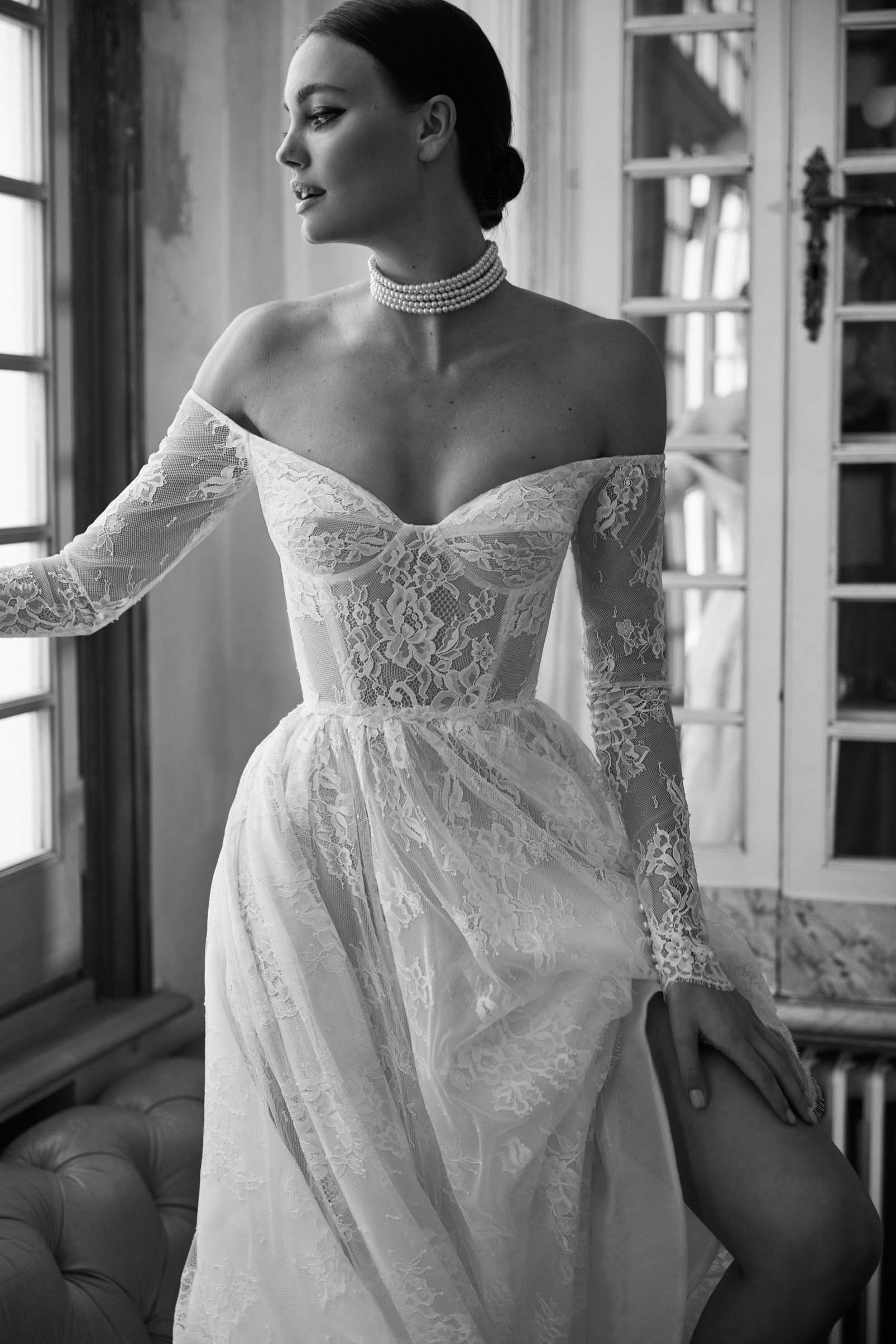 A black and white photo of a woman in a wedding dress standing next to a window.