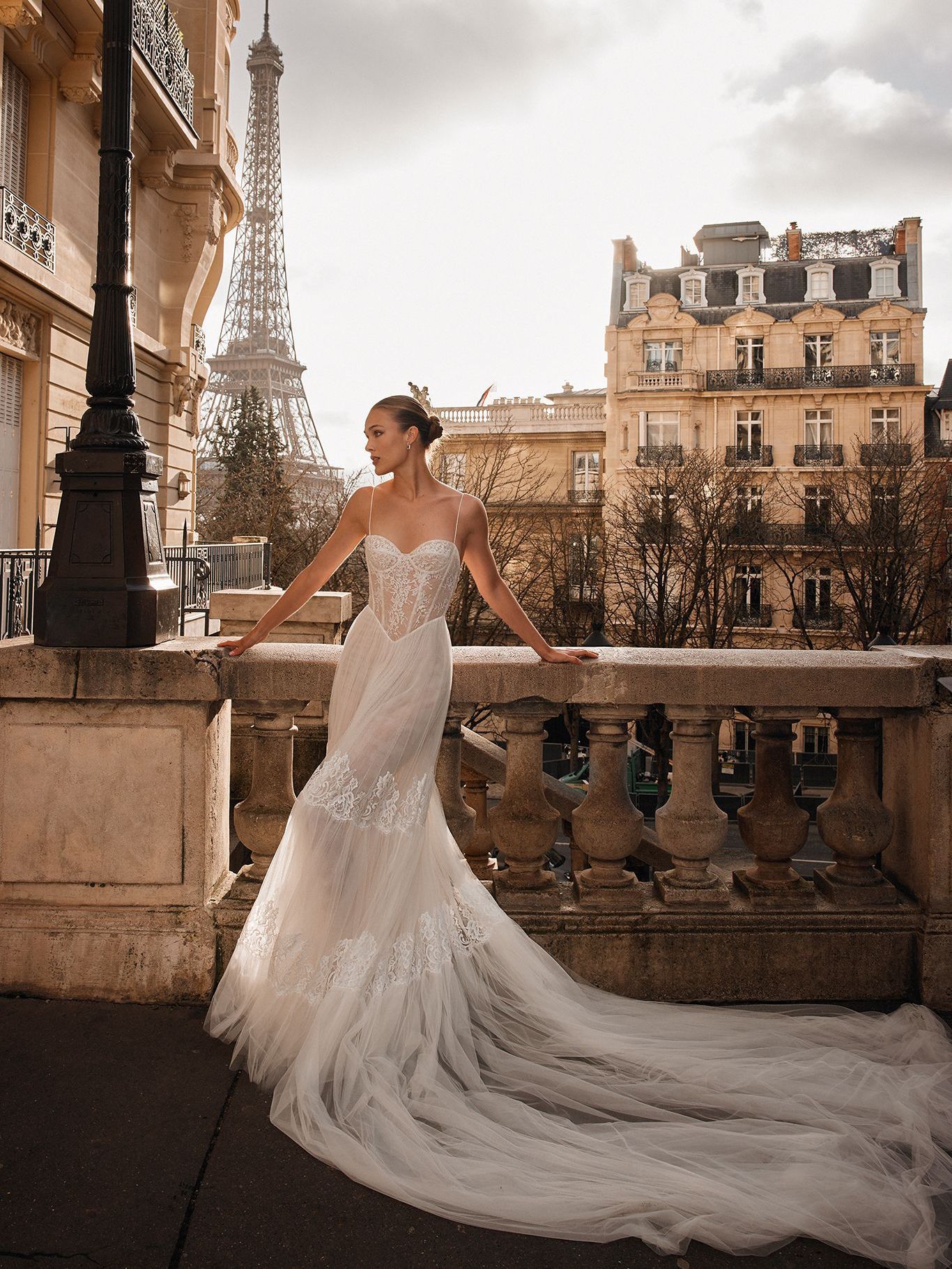 A woman in a wedding dress is leaning on a railing in front of the eiffel tower.