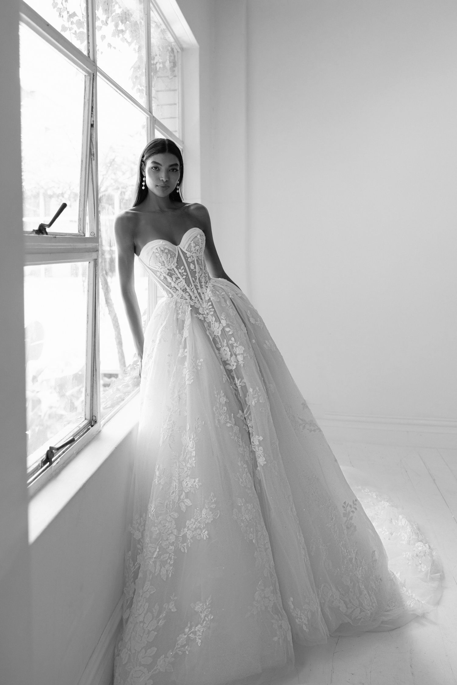 A woman in a wedding dress is standing in front of a window.