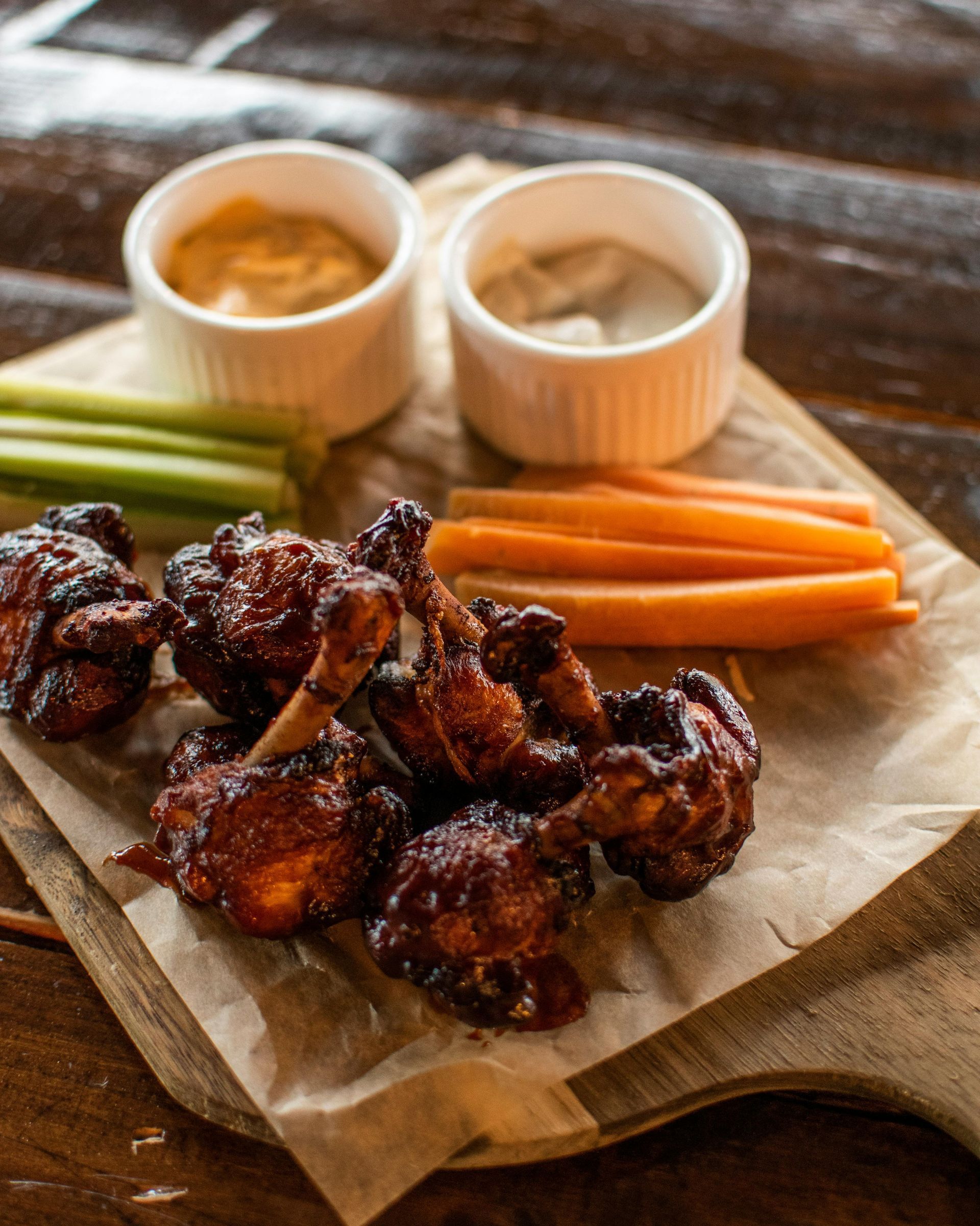 Chicken wings with dipping sauces, celery, and carrots on a wooden board.