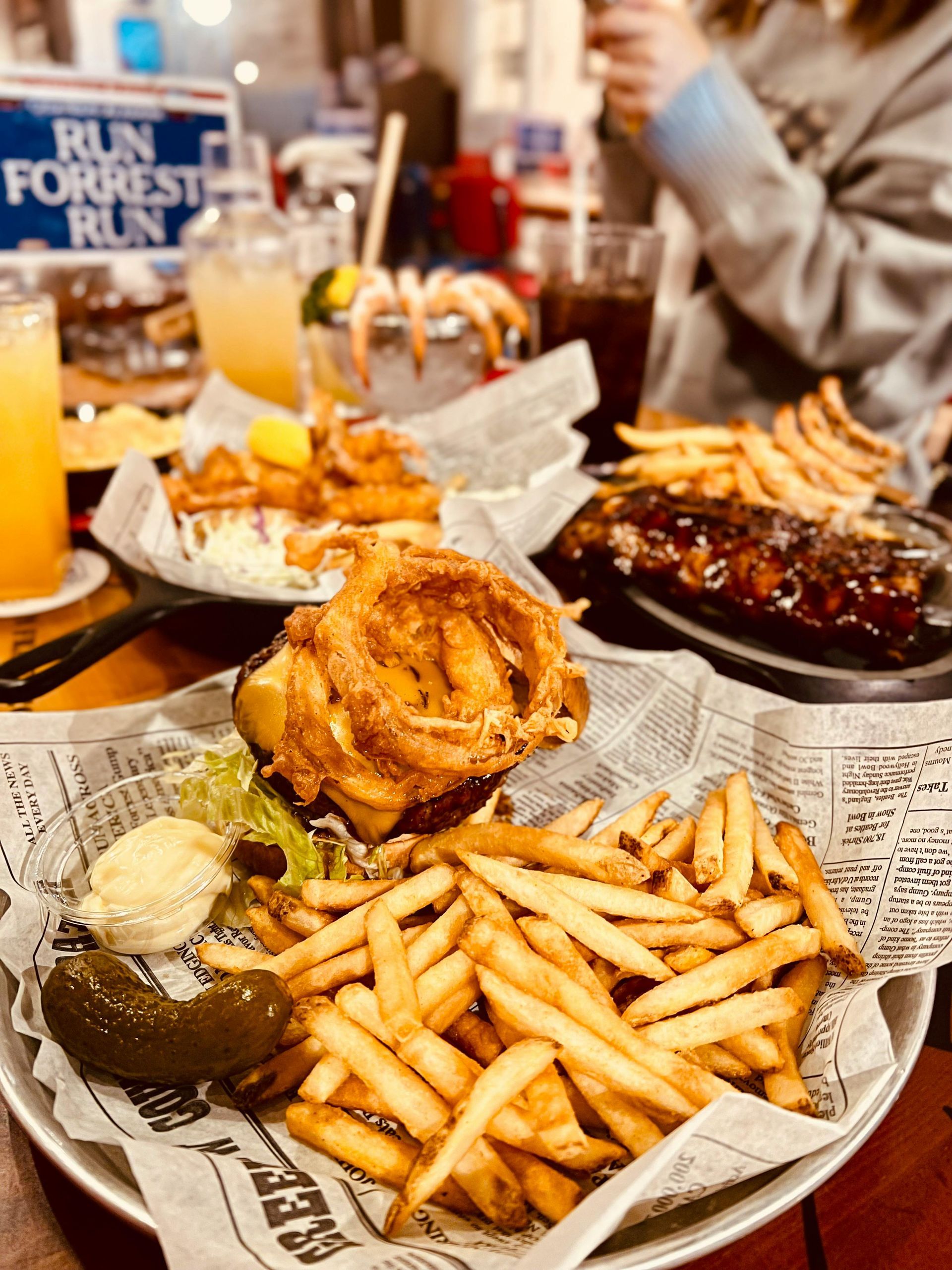 Burger with onion rings and fries, ribs, shrimp cocktail, and other dishes on a table in a restaurant.