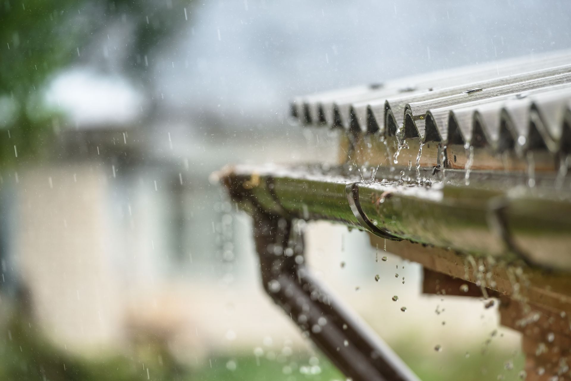 Rain is falling from the roof of a house into a gutter.