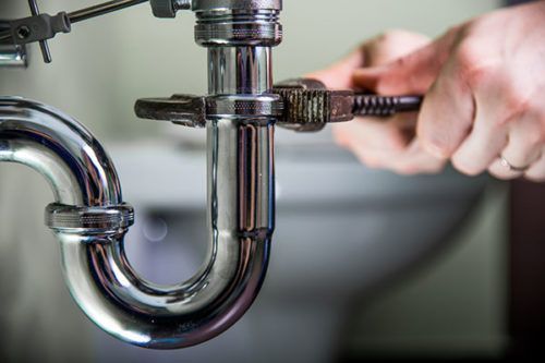 a plumber is fixing a sink pipe with a wrench .