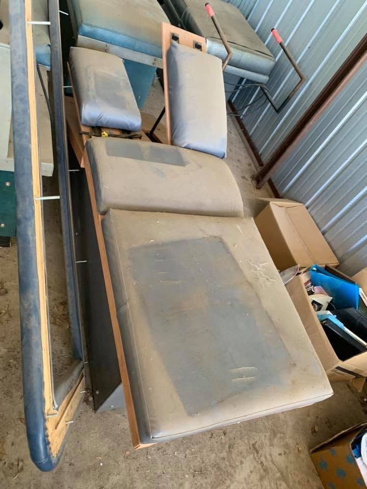 Dusty outdoor couch cushions stacked beside corrugated metal walls in a cramped storage area