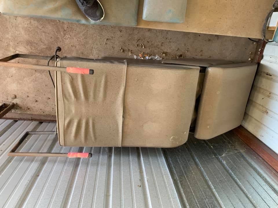 Brown sofa and cushions on a corrugated metal floor against a wall, viewed sideways.