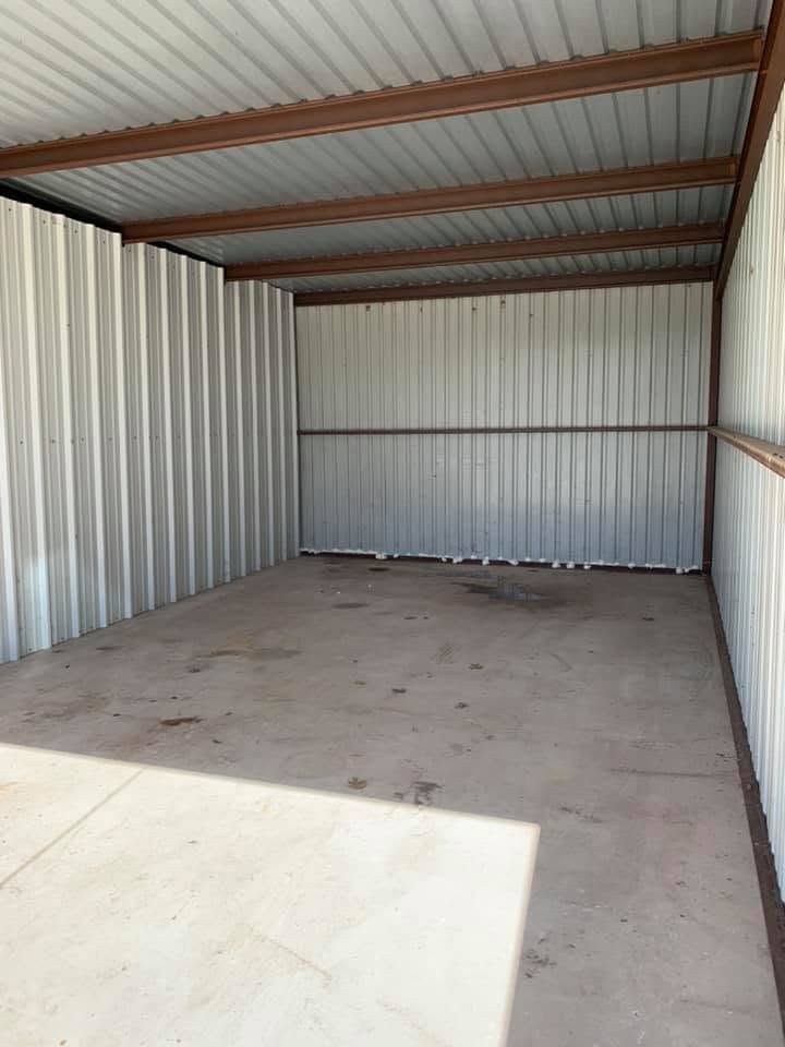 Empty metal storage unit with corrugated walls, concrete floor, and a partially open doorway letting in sunlight