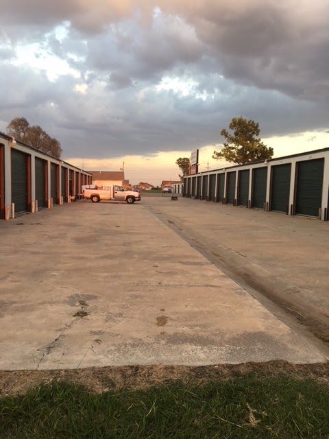 Storage units lining a wide concrete driveway under a cloudy sky, with a van parked in the distance.