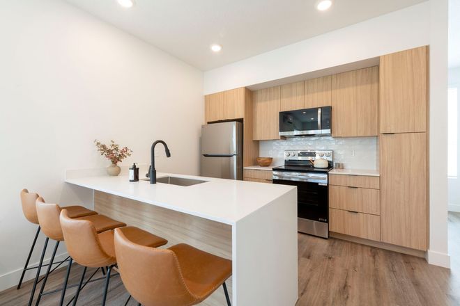 A modern kitchen with a white island, brown bar stools, light wood cabinets, and stainless steel appliances.