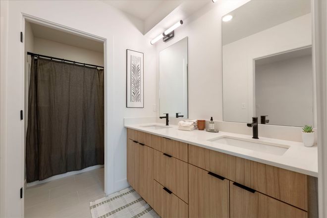 A modern bathroom with a double vanity, large mirrors, and a shower with a dark curtain.