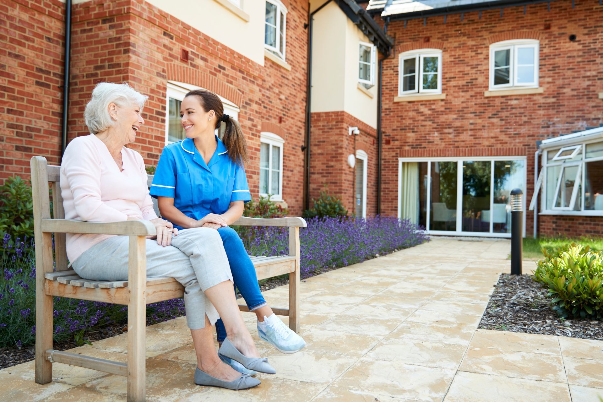 Angel's Touch Care assisted living facility serving Ellicott City, MD seniors Two people sitting on a bench in a brick courtyard outside a building