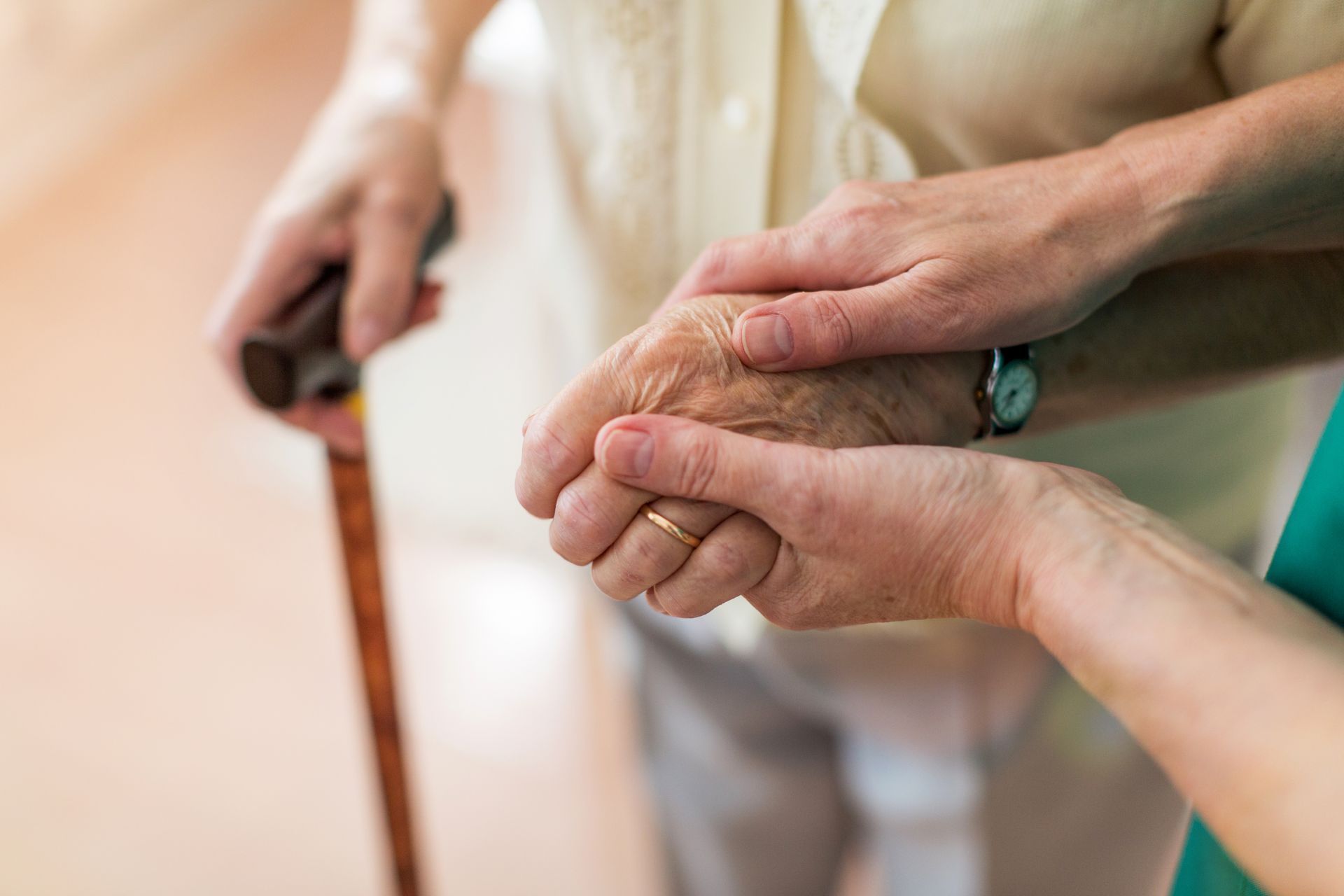 Caregiver with patient Hands of a caregiver gently holding an elderly person’s hand beside a wooden cane