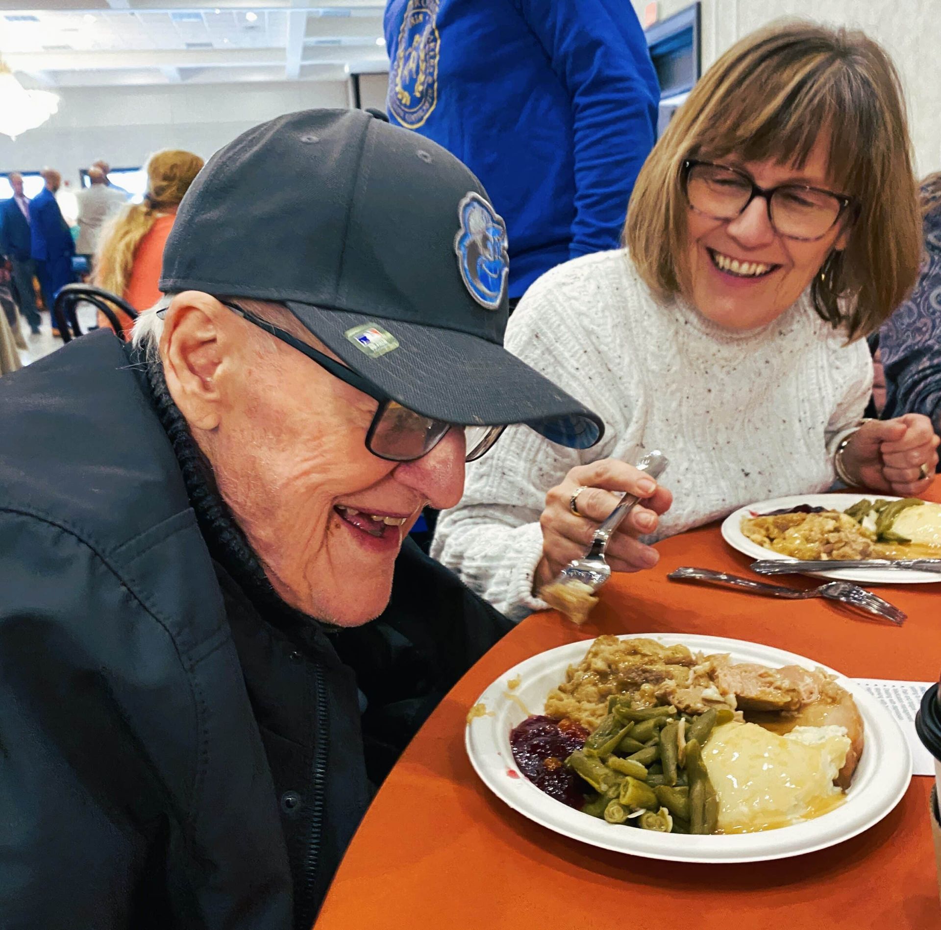 Two people smiling at a table with plates of food in a bright dining hall