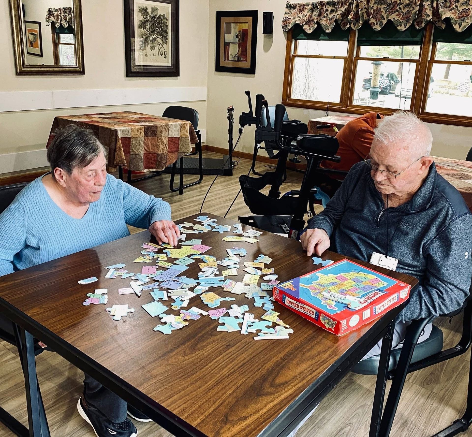 Two people play a tile game at a table in a cozy living room.