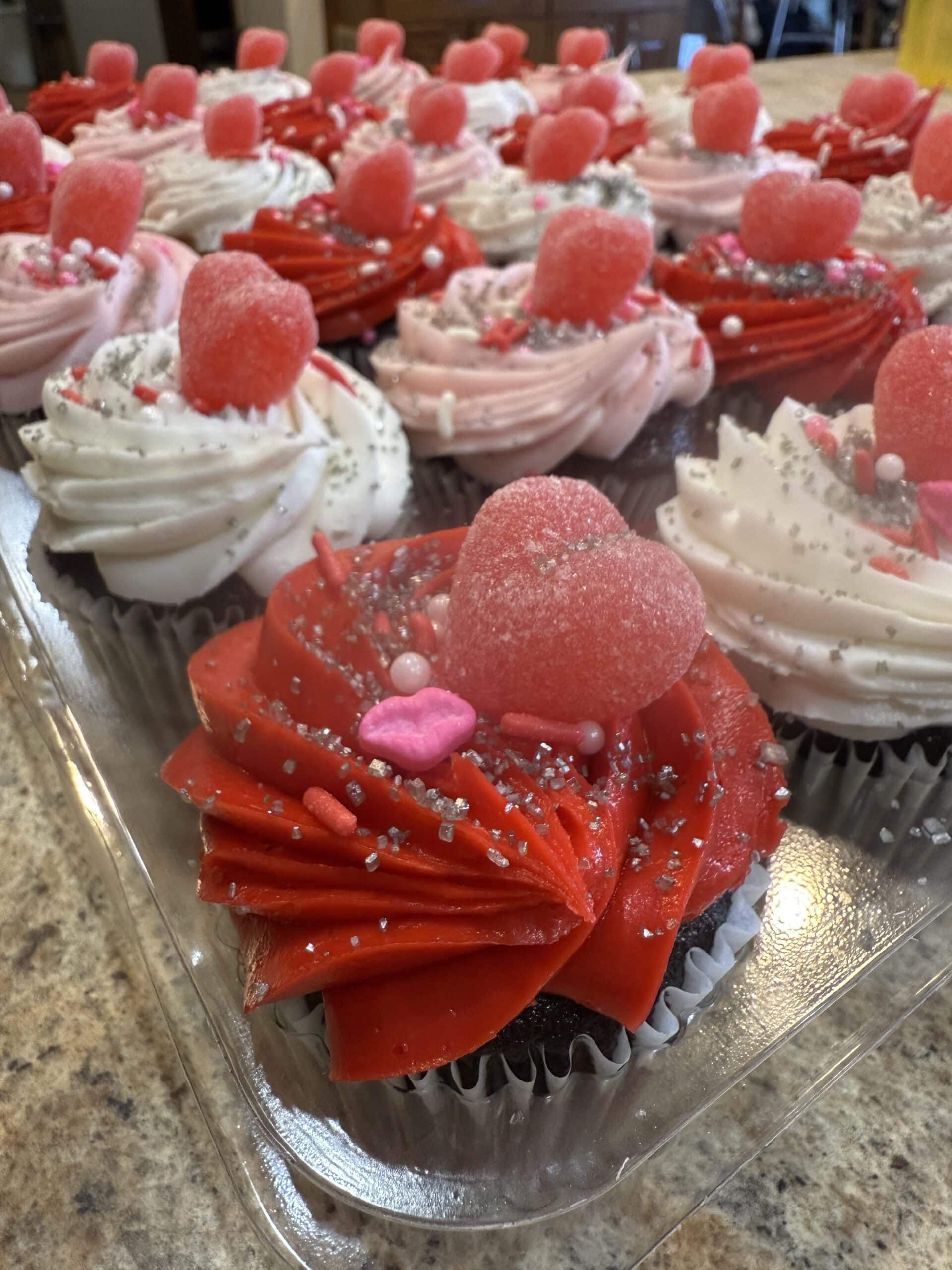 Assorted cupcakes with pink and white frosting, topped with heart decorations, displayed on a tray.