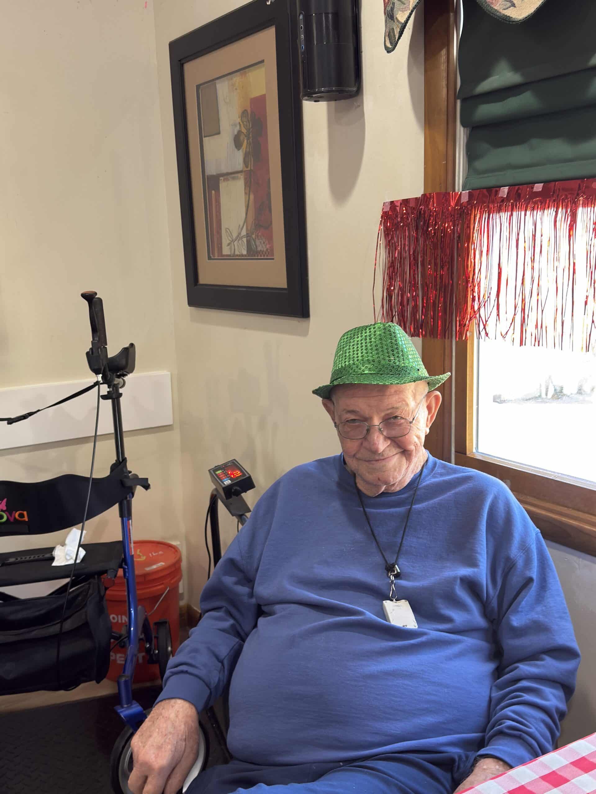 Man in green hat seated indoors beside a microphone and framed wall art