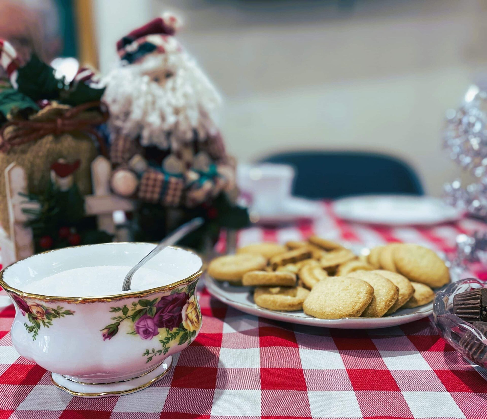 Holiday cookies and a floral teacup on a red-and-white checkered tablecloth with festive decorations in the background