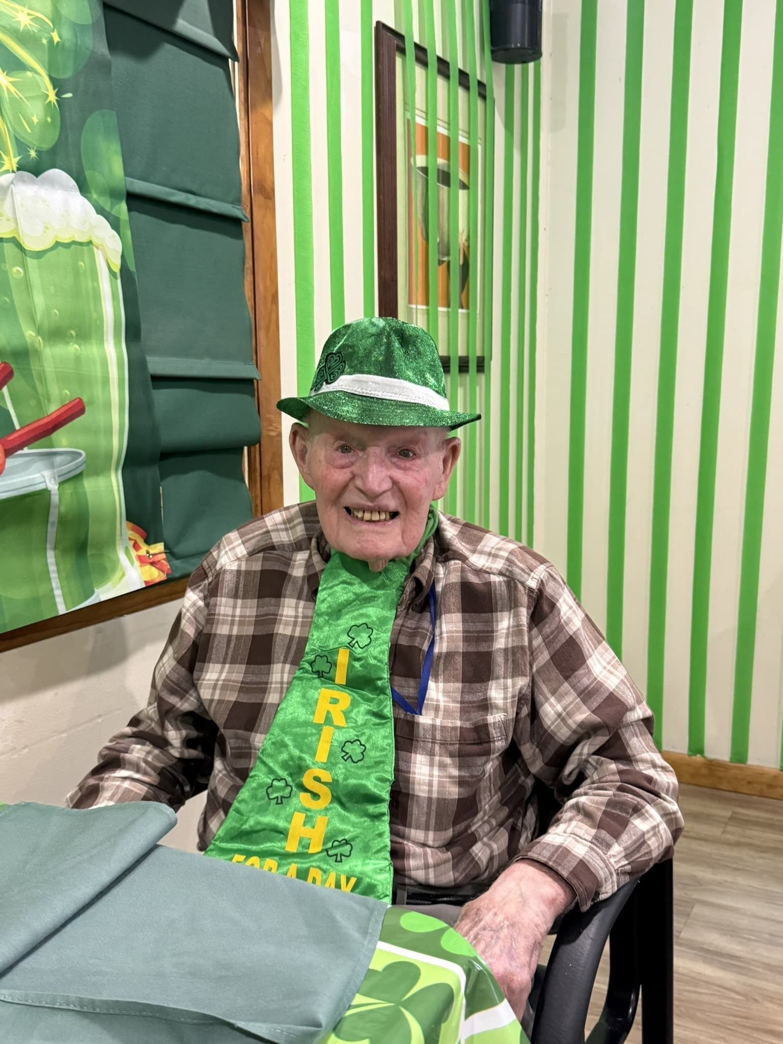 Smiling person in green hat and tie seated at a table in a decorated room.