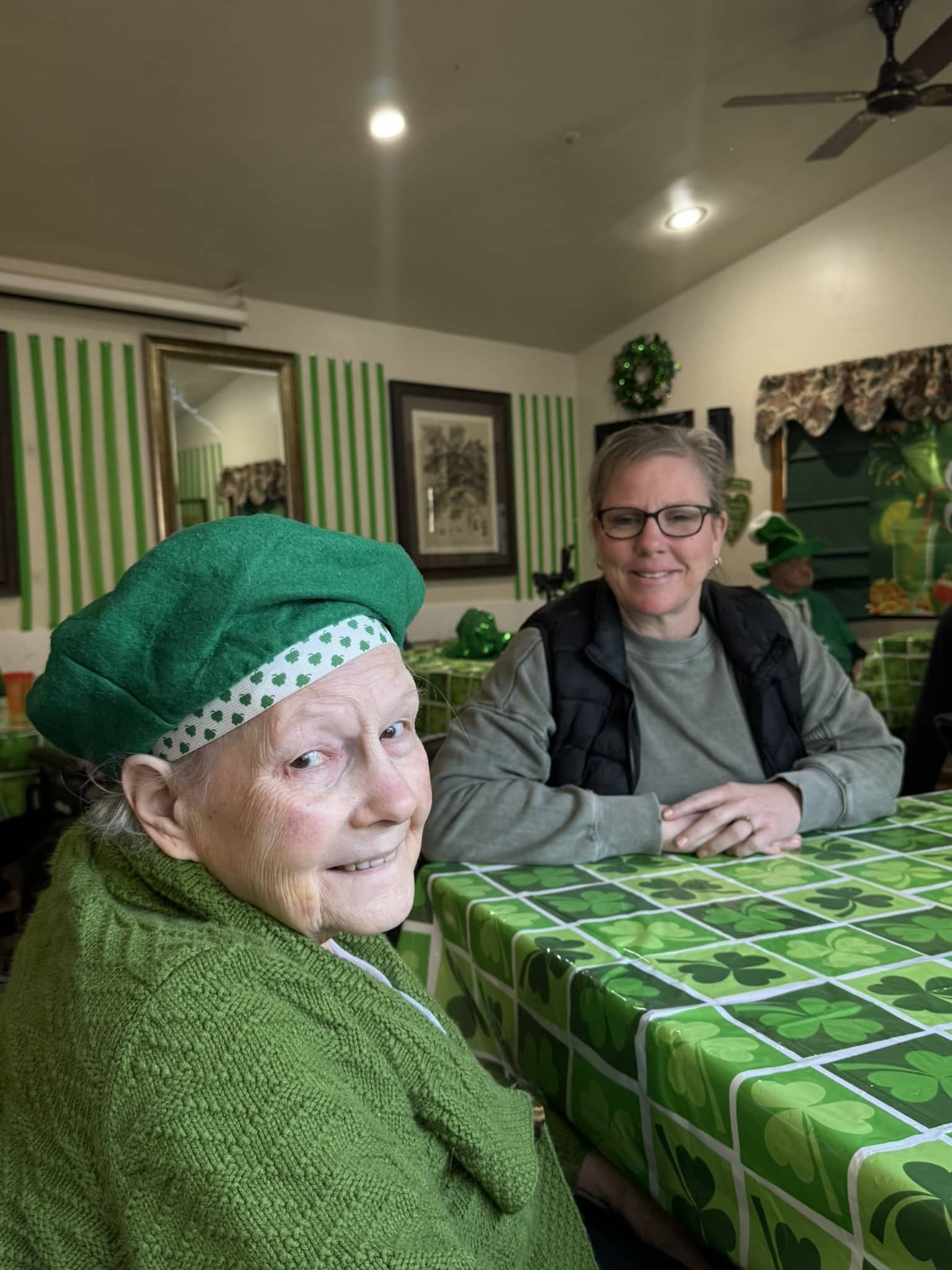 Two people seated at a green-checkered table in a cozy, striped-wall restaurant; one smiles at the camera.