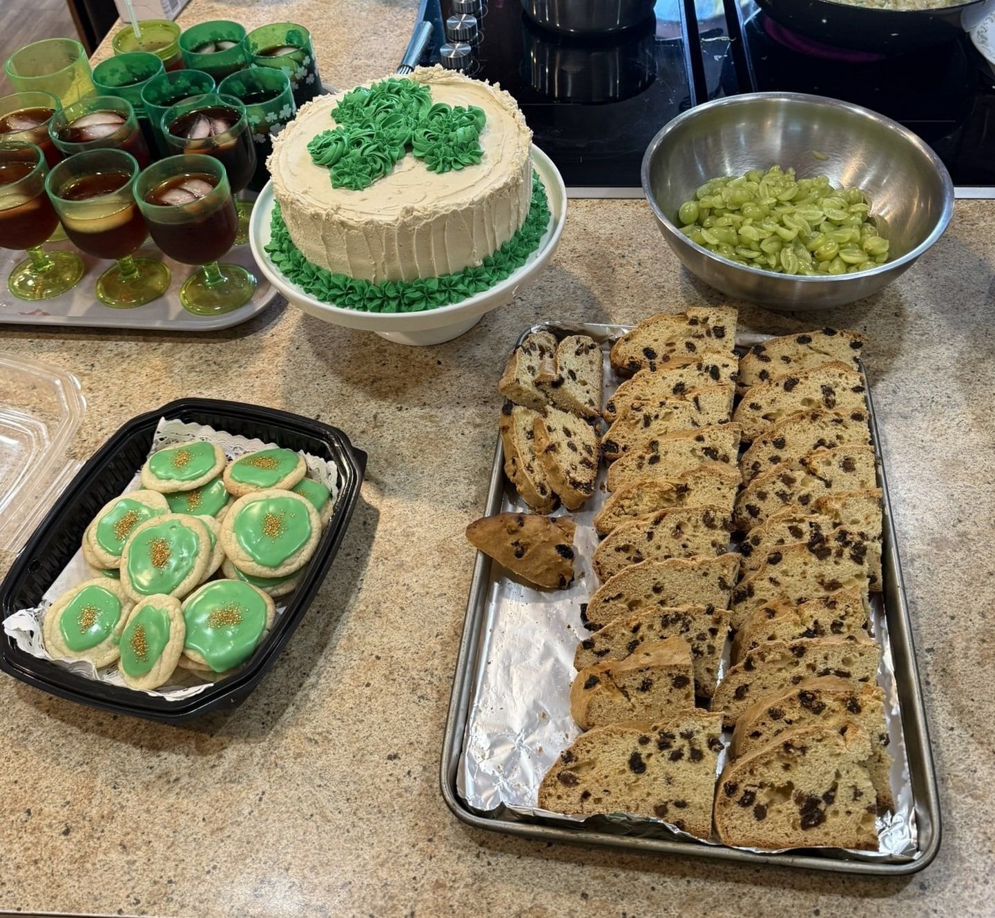 Assorted green and brown desserts on trays and bowls, including cake, rolls, and cups, arranged on a countertop