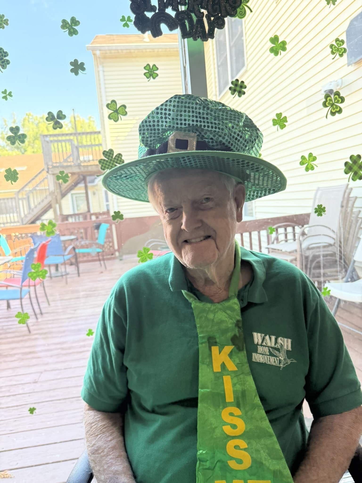 Person in green KISS shirt and shamrock hat smiling at an outdoor St. Patrick’s Day event