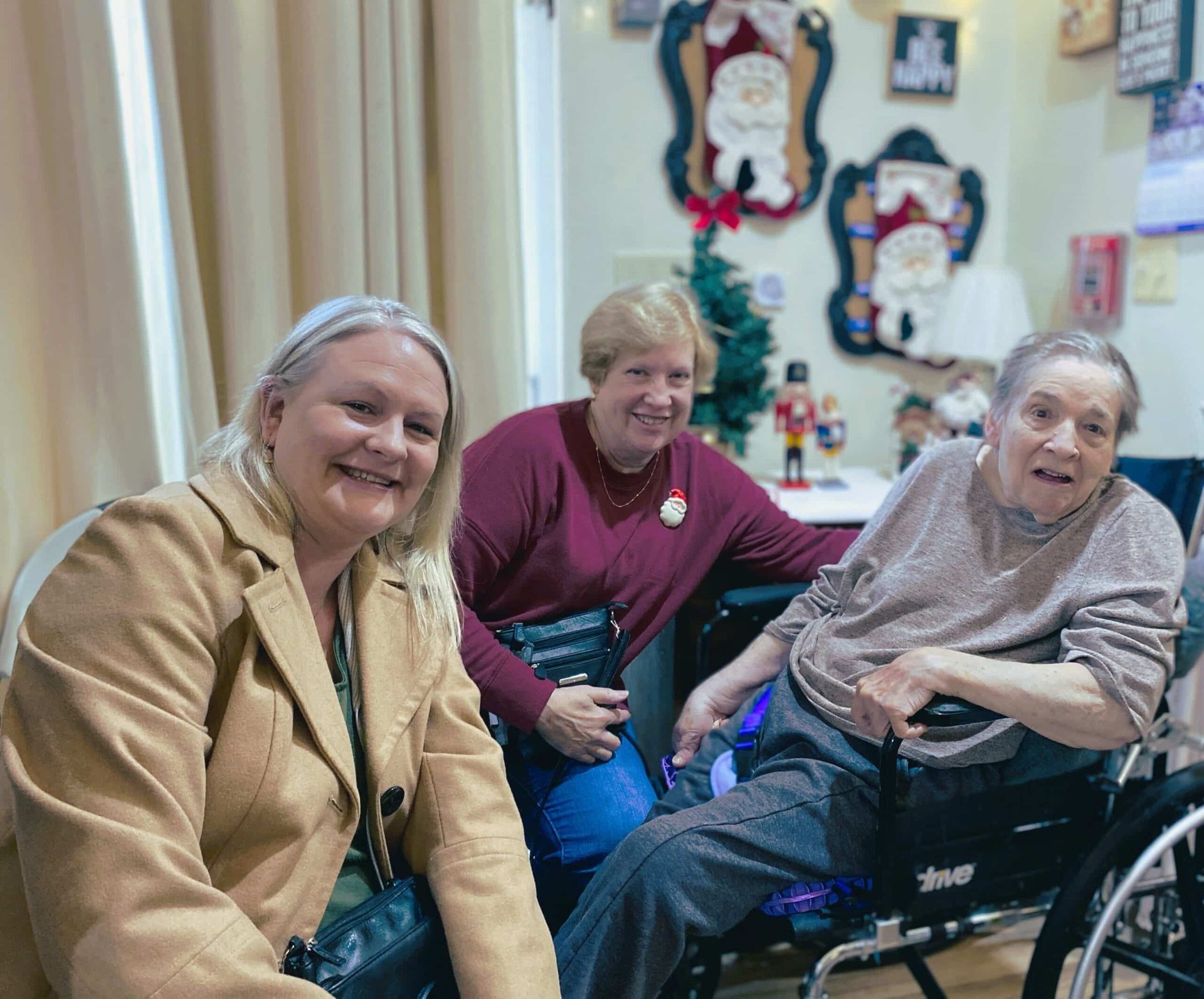 Three people smiling together in a cozy room, two seated and one in a wheelchair.