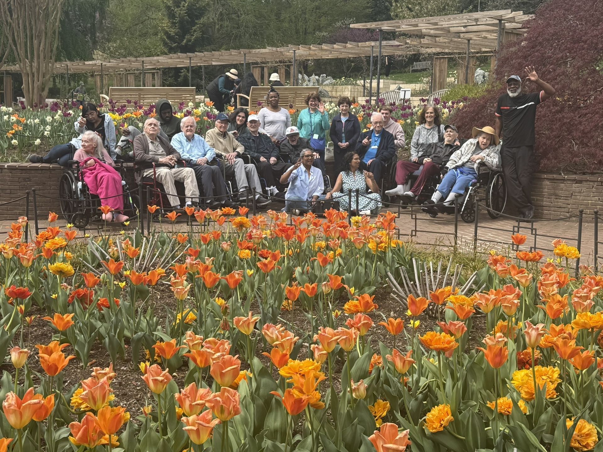 People seated in a garden behind a field of orange tulips, with a speaker standing at the right.