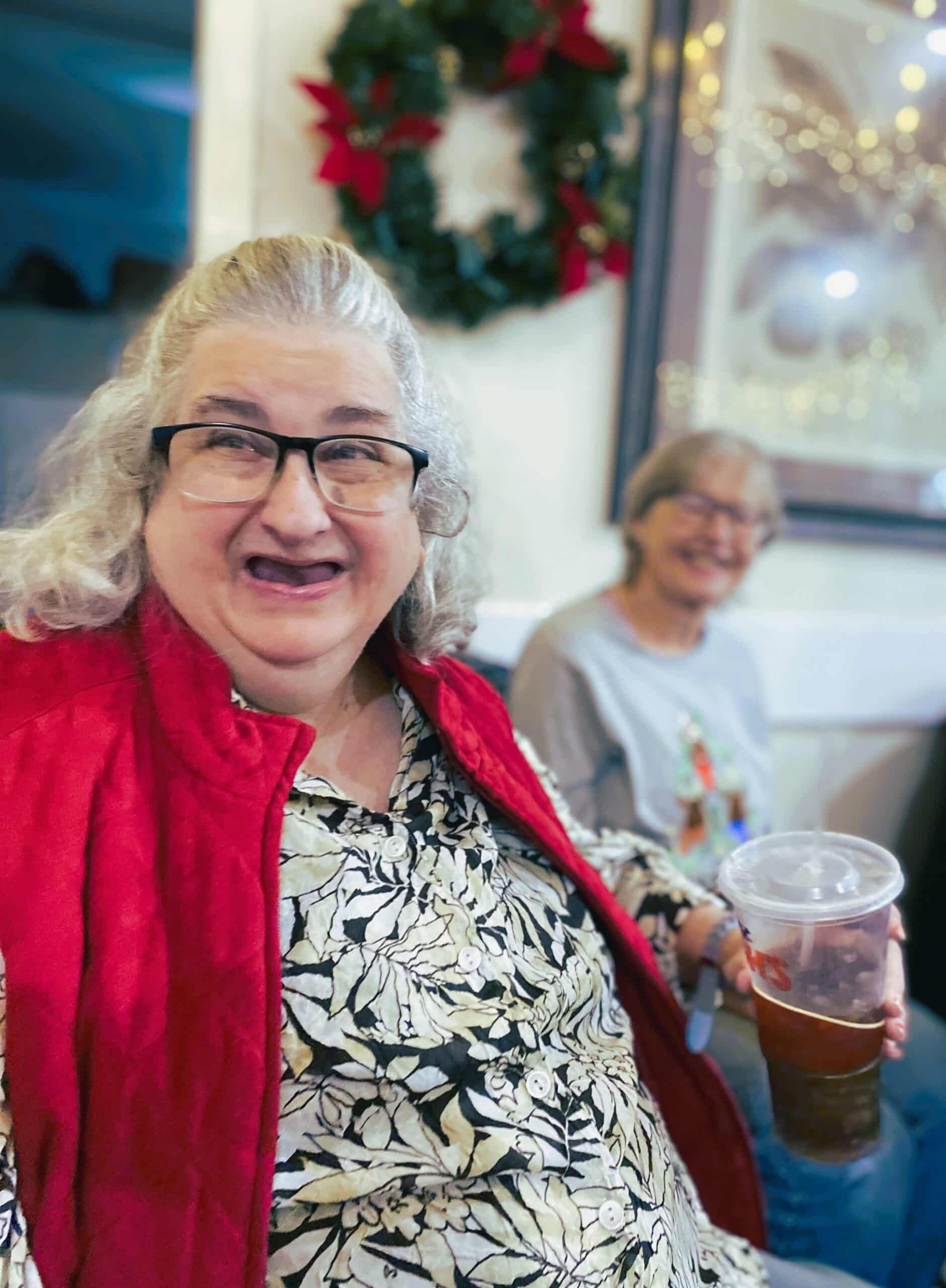 Smiling woman in red cardigan holding an iced drink at a festive indoor gathering