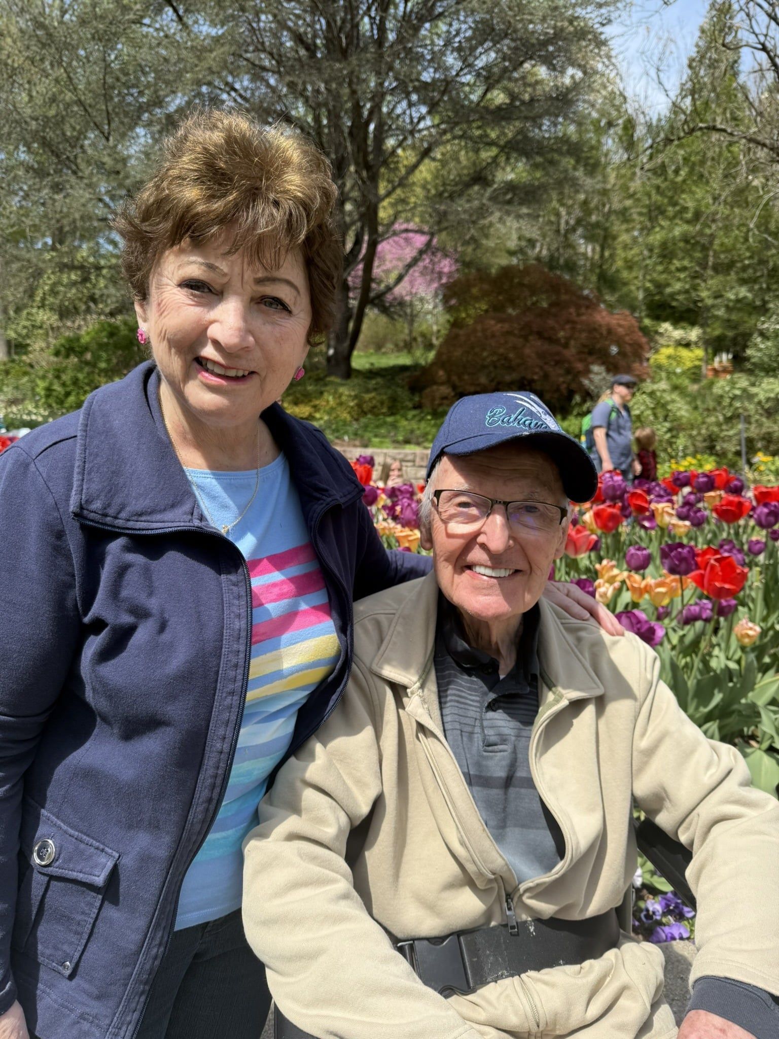 Two smiling people sitting among colorful flowers in a sunny garden