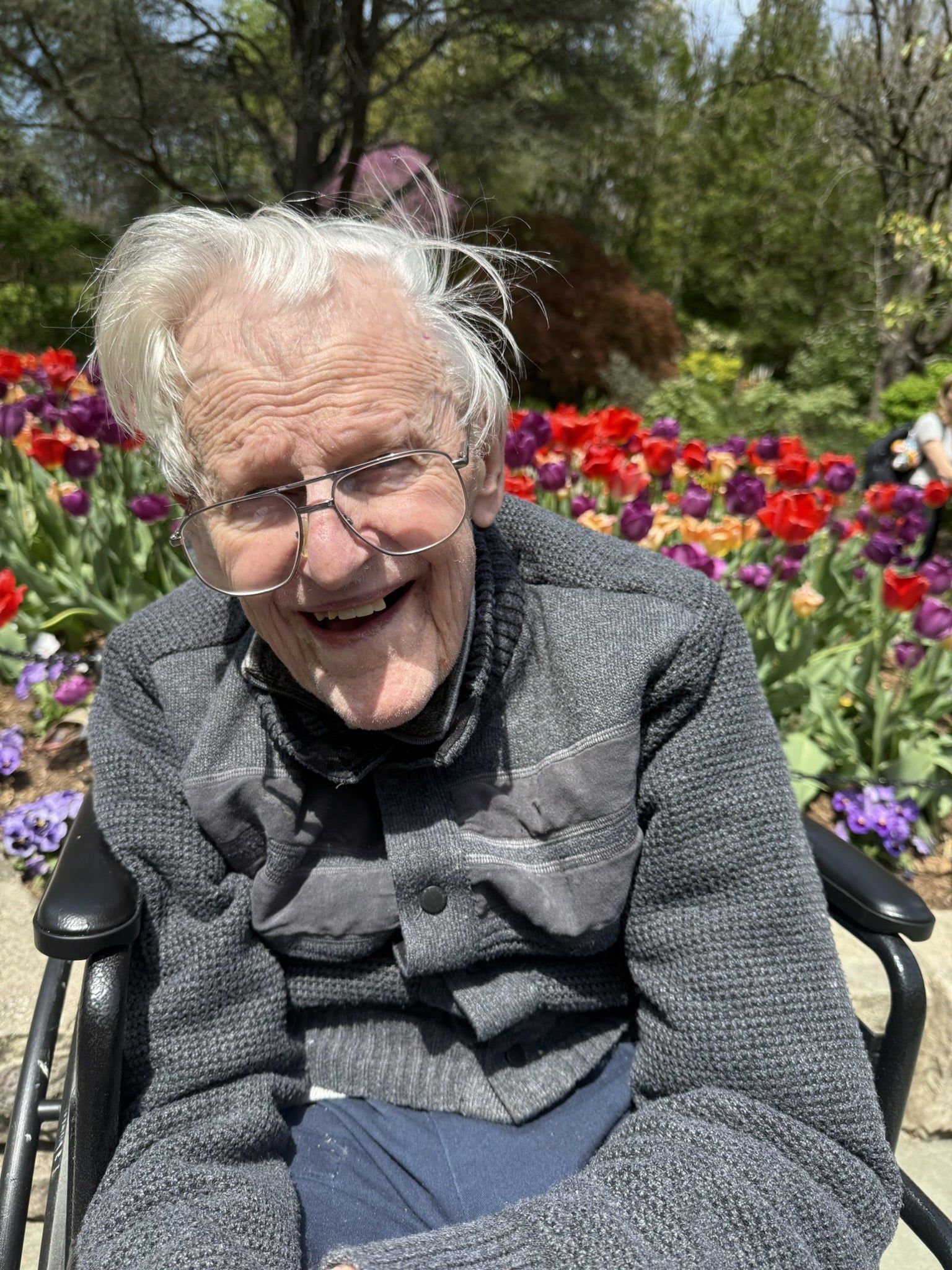 Smiling person in a wheelchair in front of colorful flowers outdoors
