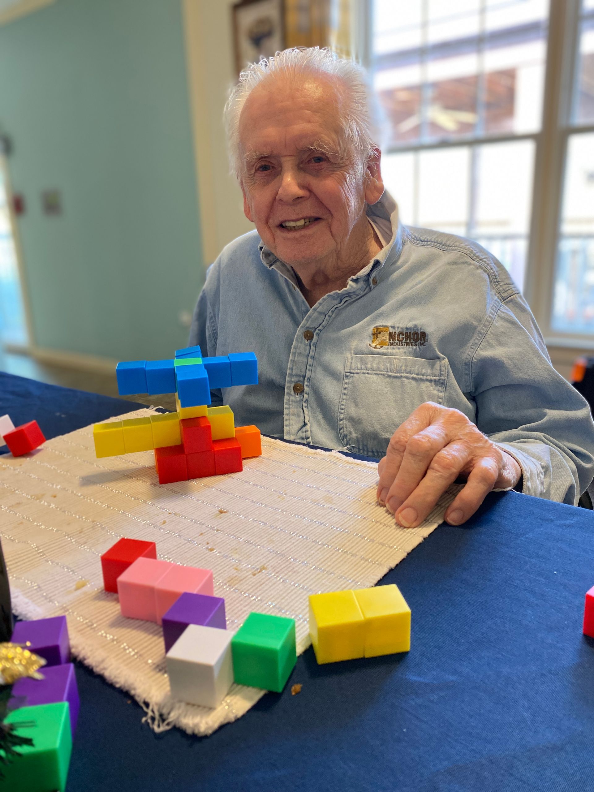 Smiling person building with colorful blocks at a table in a bright room