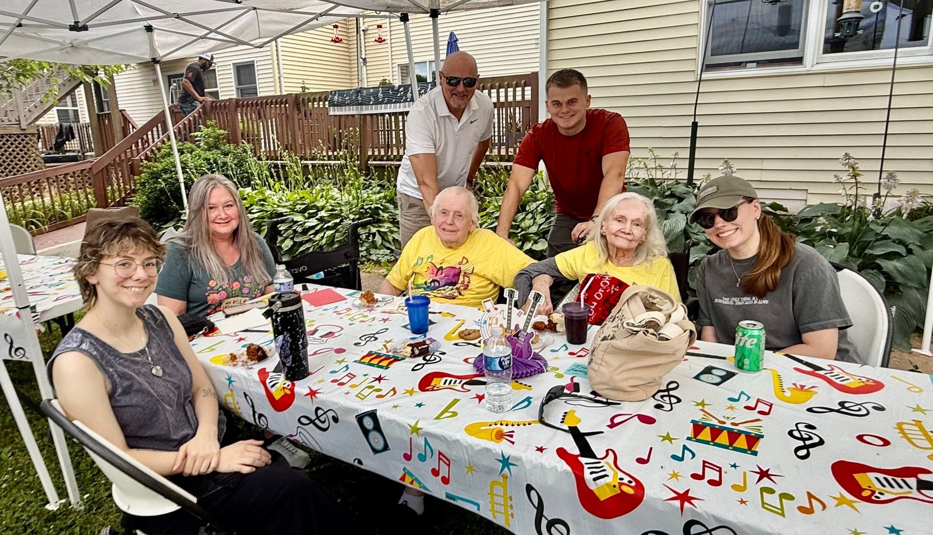 Group of people seated around a festive outdoor table with colorful decorations and drinks
