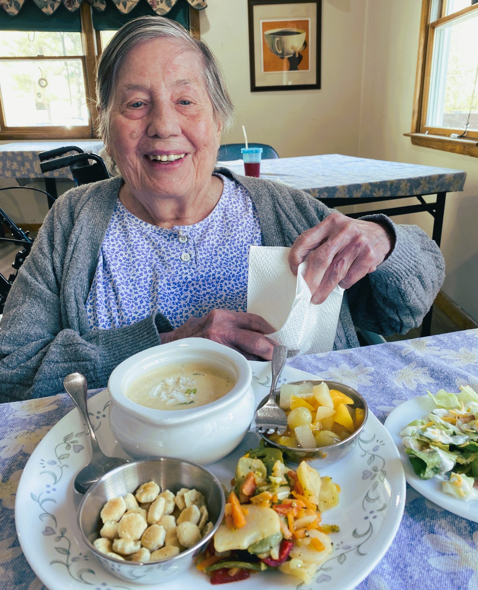 Smiling woman at a table with soup, fruit, and salad in a bright dining room