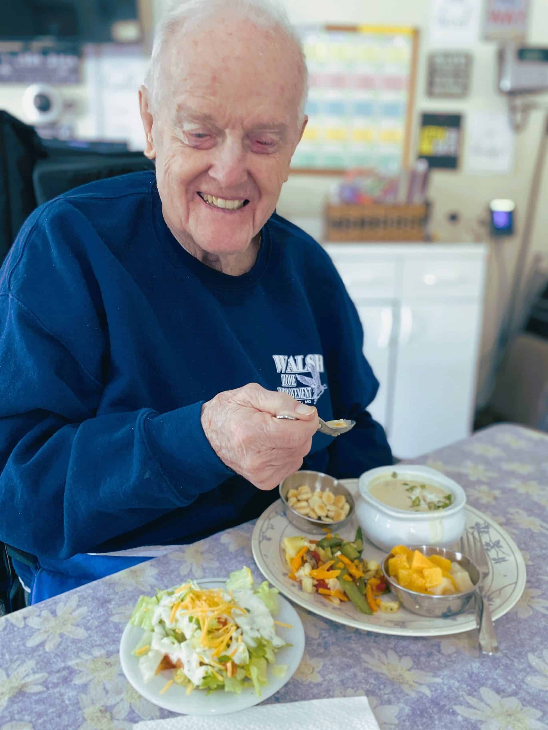 Smiling person in a blue sweater eating a meal at a table with several bowls and plates