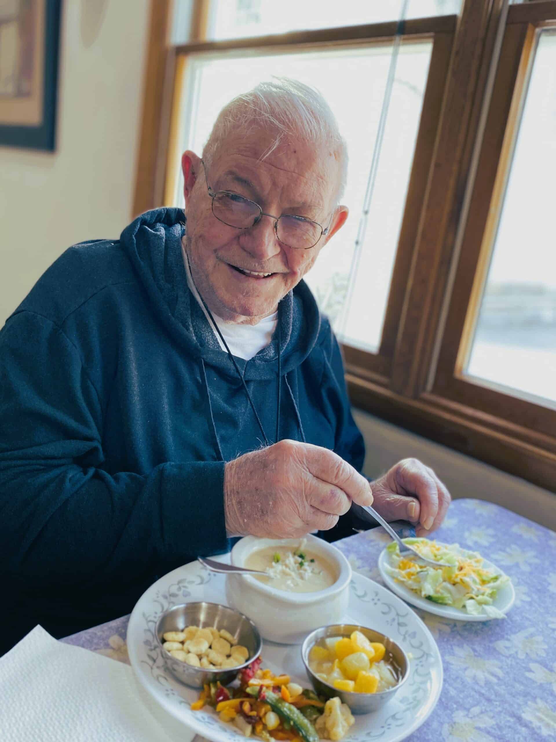 Person in a blue hoodie eating a meal by a window, with several small bowls of food on the table.